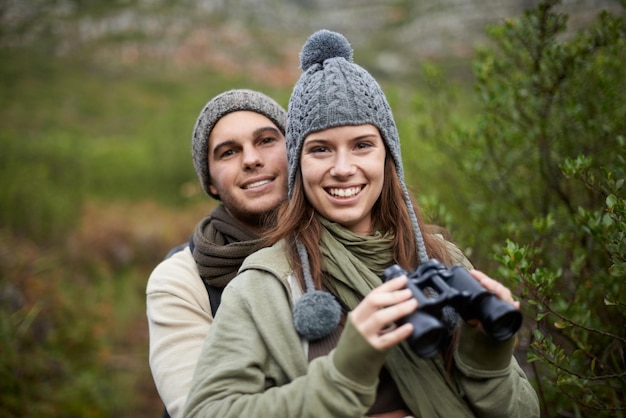 Wanderporträt, Fernglas und Lächeln des Paares für die Natur, Wochenendausflug und Camping-Retreat im Öko-Wald, nachhaltige Wälder, Liebe und Menschen, die sich auf Reisen, Abenteuer, Trekking oder Vogelbeobachtung verbinden.