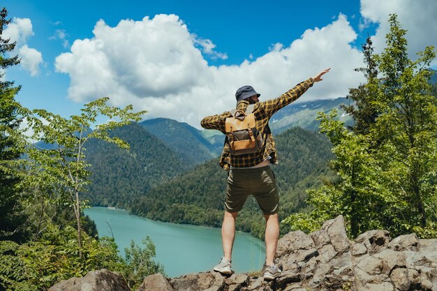 Wanderreisender Mann mit erhobenen Rucksackhänden genießt die schöne Aussicht auf den Ritsa-See in Abchasien