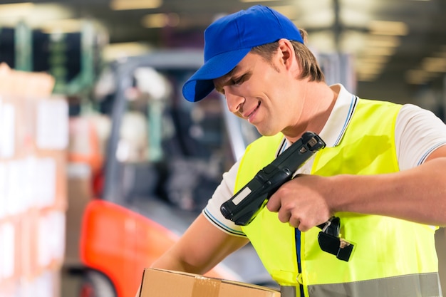 Warehouseman com colete de proteção e scanner, verifica o código de barras do pacote, ele está no armazém da empresa de expedição de mercadorias