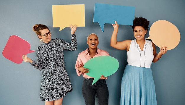 Waren alle für Humor und Spaß Studioaufnahme einer Gruppe attraktiver junger Geschäftsfrauen, die Sprechblasen halten, während sie vor einem grauen Hintergrund stehen