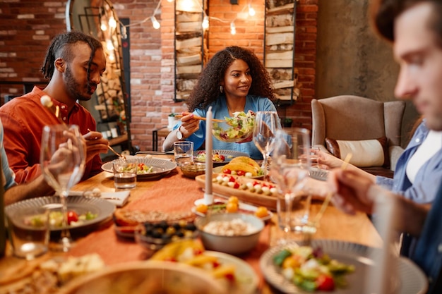 Warm getöntes Porträt verschiedener junger Menschen, die eine Dinnerparty am Tisch in gemütlicher Umgebung genießen