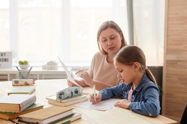 Warm getöntes Seitenansichtporträt des niedlichen kleinen Mädchens, das Test schreibt, während zu Hause mit Mutter oder Tutor studiert, die ihr helfen, Raum zu kopieren