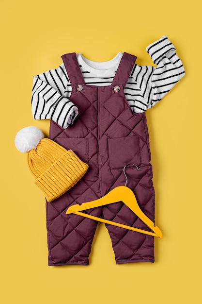 Warme Hose und gestreifter Pullover mit Hut auf gelbem Grund. Set Babykleidung für den Winter. Mode Kinder Outfit.