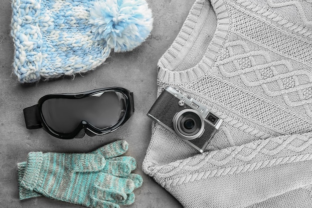 Warme Kleidung mit Fotokamera und Skibrille auf grauem Hintergrund Winterurlaubskonzept