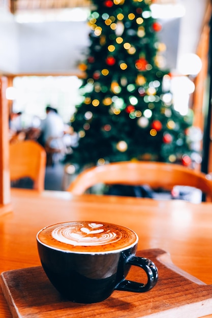 Warme Tasse Kaffee auf dem Hintergrund des Weihnachtsbaums mit Lichtern