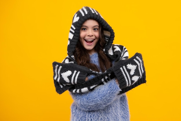 Warmer Hut mit Kapuze und Schal Amazed Teenager Schönes jugendlich Mädchen in einem Winterhut und in einem warmen Pullover Ein Kind auf einem gelben isolierten Hintergrund Aufgeregtes jugendlich Mädchen