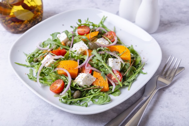 Warmer Salat mit Kürbis, Feta, Tomaten, Kapern, Rucola und roten Zwiebeln.