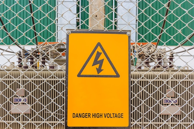 Warnschild auf einer Baustelle mit Hochspannungstransformatoren im Hintergrund