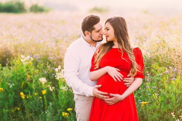 Warten auf das Baby Paar erwartet ein Baby Mann umarmt und küsst eine schwangere Frau Zukünftige Eltern Schwangerschaft Kerl umarmt ein schwangeres Mädchen an einem hellen sonnigen Herbsttag auf einer grünen Wiese mit Gras