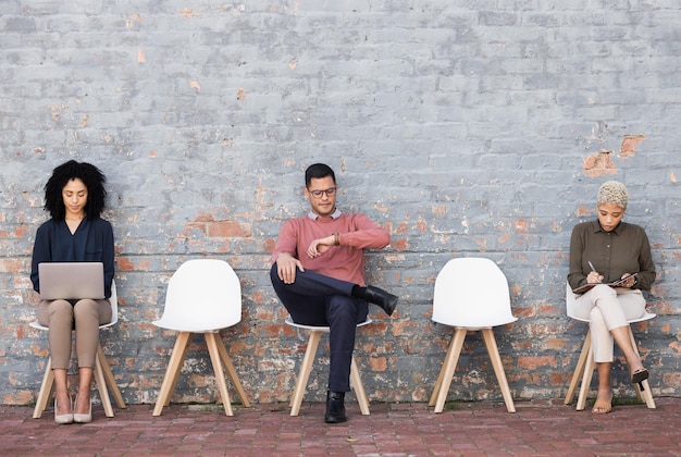 Wartezimmer von Geschäftsleuten und sitzen auf Stühlen an der Ziegelwand für ein Vorstellungsgespräch oder eine Gelegenheit Gruppe kreativer Praktikanten in sozialer Distanzierung und Überprüfung der Zeit für den Start
