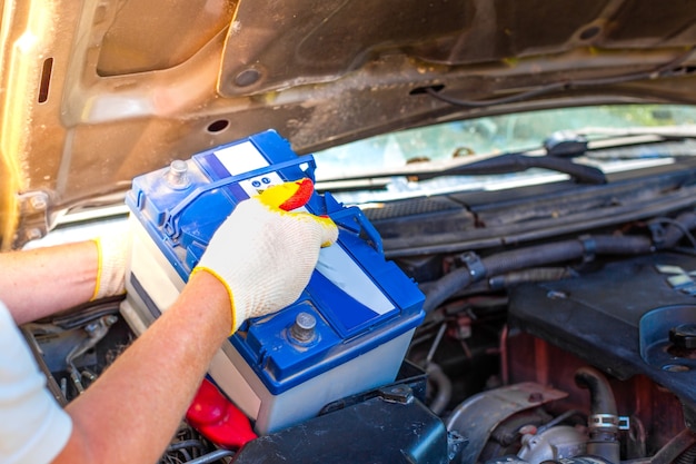 Wartung der Maschine. Ein männlicher Automechaniker nimmt eine Batterie unter der Motorhaube eines Autos heraus, um sie zu reparieren, aufzuladen oder zu ersetzen.