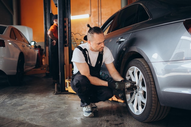 Wartung männlicher Reifenüberprüfungsdienst über das Versicherungssystem in der Garage Sicherheitsfahrzeug zur Verringerung von Unfällen vor einer langen Reise Blaues Auto des Mannes Transportlebensstil