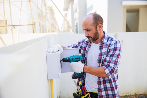 Wartungsservice Reparatur- und Handwerkerkonzept Hispanischer männlicher Elektriker-Ingenieur Installateur mit elektrischem Bohrwerkzeug in seinen Händen