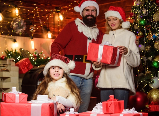 Was befindet sich im Inneren des kleinen Kindes und der Eltern in Weihnachtsgeschenkboxen mit Weihnachtsmütze Öffnen Sie das Geschenk Winterferien