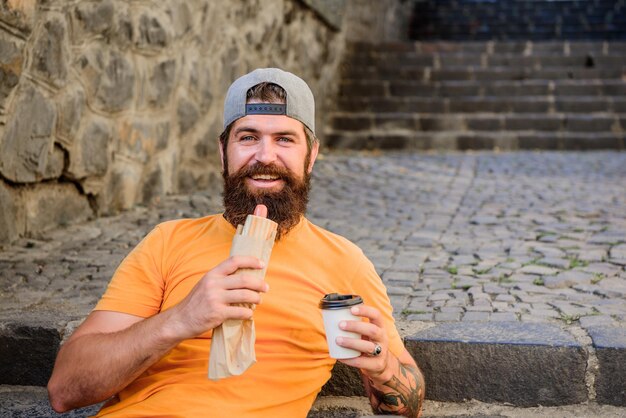 Was für ein Snack Bärtiger Mann, der ungesunden Hotdog-Sandwich-Snack isst Hipster ruht und hat Hotdog-Snack auf der Treppe im Freien