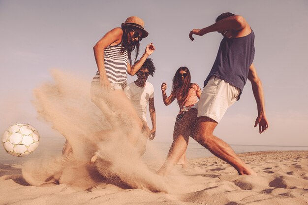 Was für ein Spiel! Gruppe fröhlicher junger Leute, die mit Fußball am Strand spielen