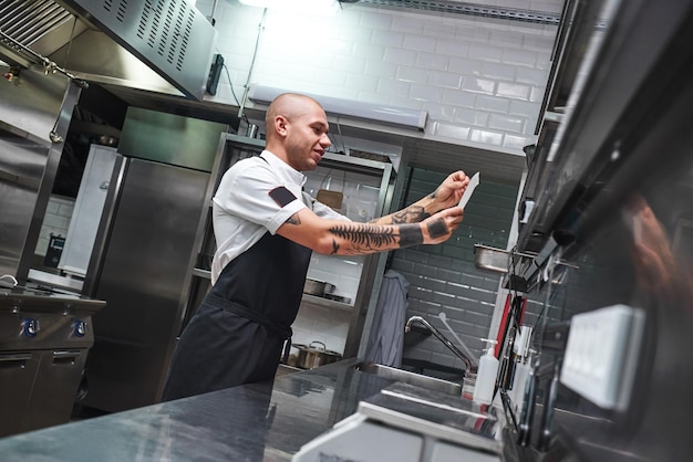 Was kommt als nächstes gut aussehender kahlköpfiger männlicher Koch mit Tattoos auf den Armen, der auf Bestellung schaut?