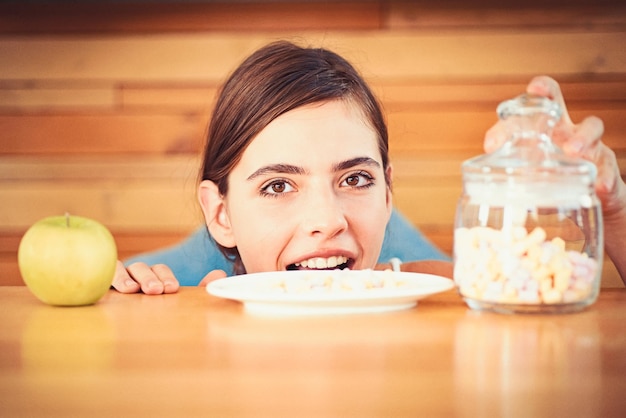 Was schmeckt besser Süß und ungesund oder organisch und natürlich Frau wählt, was sie essen soll Hübsche Frau, Blick auf Apfel und Marshmallows Diätetische oder ungesunde Lebensmittel Vitamin oder Zucker