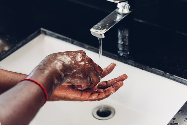 Waschen der Hände eines schwarzen Mannes mit Seife und Wasser in Waschbecken, um den Ausbruch des Coronavirus zu verhindern