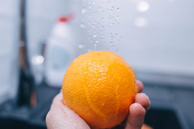 Waschen einer Orange unter fließendem Wasser nasses Obst