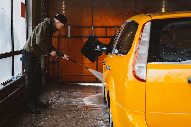 Waschen eines gelben Autos in einer kontaktlosen Selbstbedienungswaschanlage Waschen eines Limousinenautos mit Schaum und Hochdruckwasser