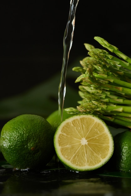 Waschen Sie Limette und Spargel mit einem Wasserstrahl und gießen Sie Wasser aus dem Wasserhahn auf die Gemüse-Nahaufnahme