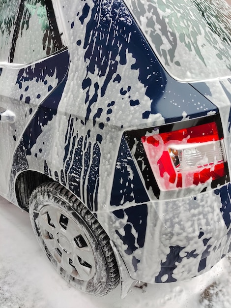 Waschschaum fließt an den Seiten des Autos herunter auf den Asphalt. Nur das Heck des Autos ist zu sehen