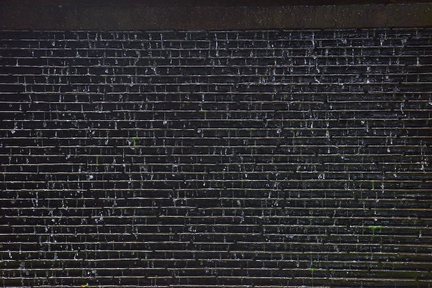 Wasser fällt auf alten grauen Wandhintergrund des Ziegelsteines.