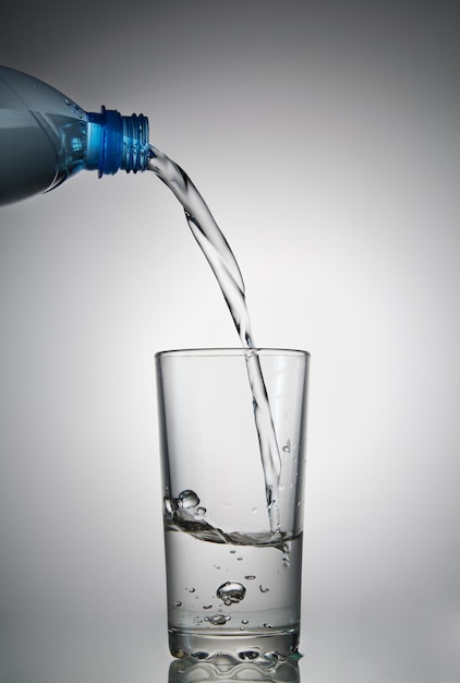 Wasser fließt in ein Glas aus einer Plastikflasche