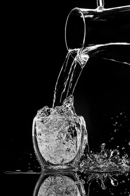 Wasser gießt aus einem Dekanter auf schwarzem Hintergrund in ein Glas