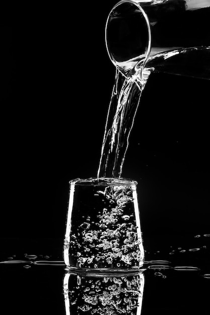 Wasser gießt aus einem Dekanter auf schwarzem Hintergrund in ein Glas