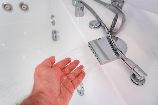 Wasser kommt aus dem Wasserhahn eines Whirlpools und die Hand eines Mannes berührt das Wasser mit seinen Fingern