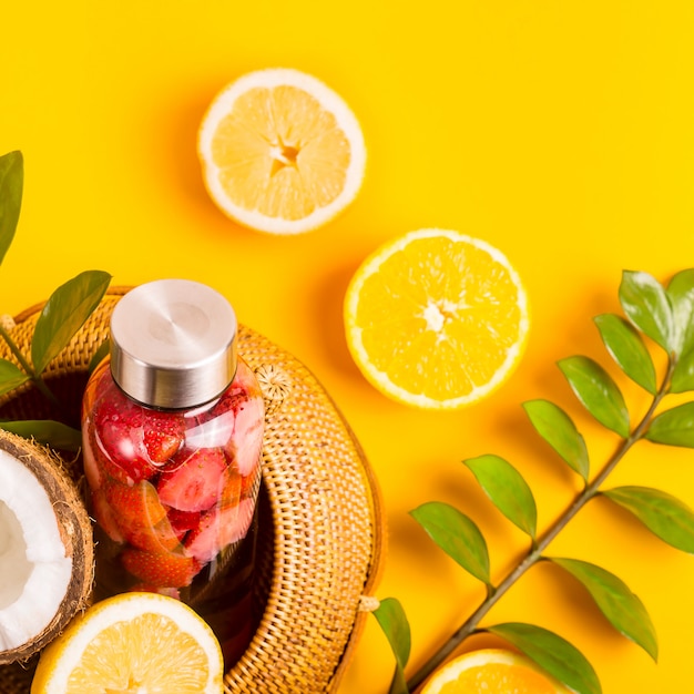 Wasser mit Erdbeeren, Orangen, Zitronen und Kokosnüssen auf Gelb mit einem Strohsack