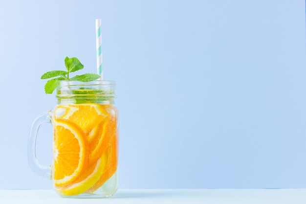 Wasser mit Orangenfrüchten auf blauem Hintergrund, eisiger Sommerzitrusgetränk in einem Glas