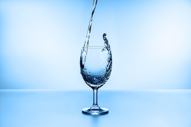 Wasser spritzt aus Glas isoliert auf blau