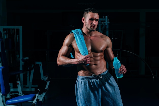 Wasser trinken Sportler ohne Hemd, der sich nach dem Training im Fitnessstudio ausruht, sitzt auf dem Boden und trinkt Wasser mit geschlossenen Augen