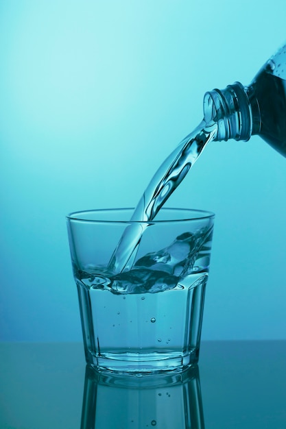 Wasser wird in ein Glas an einer blauen Wand in Nahaufnahme gegossen
