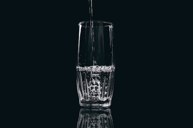 Wasser wird in ein Glas auf schwarzem Hintergrund gegossen