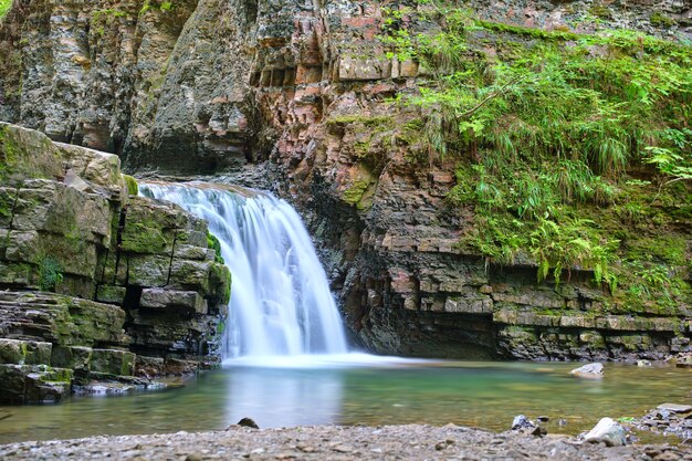 Wasserfall am Bergfluss mit weißem Schaumwasser, das von der Felsformation im Sommerwald herunterfällt.