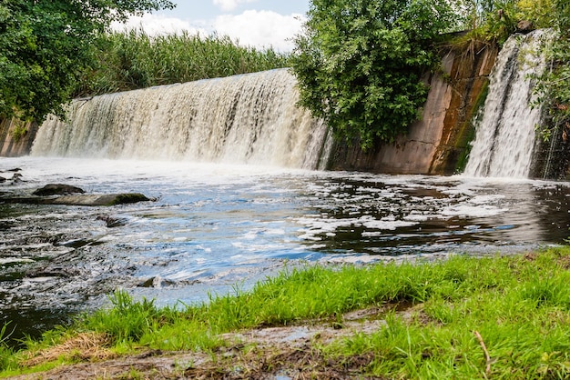 Wasserfall auf einem Hintergrund des grünen Grases und des blauen Himmels