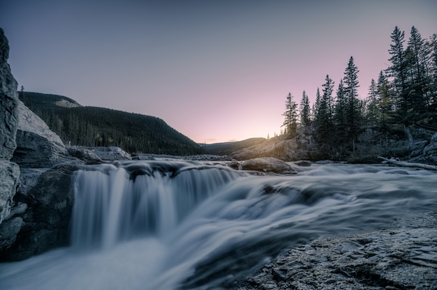 Wasserfallstromschnellen, die auf Felsen in Wald am Abend fließen