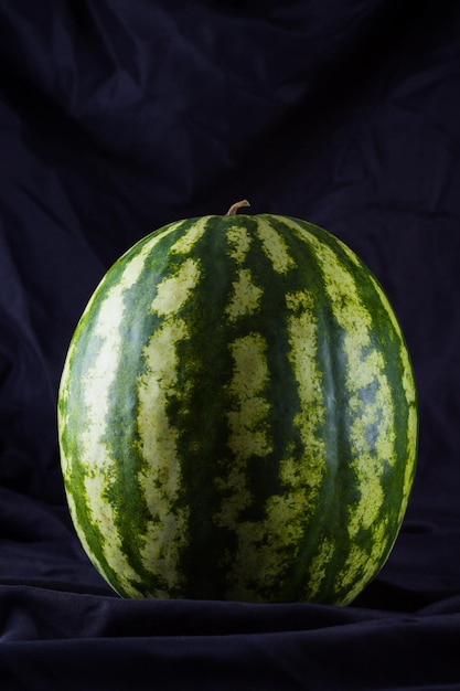 Wassermelone auf schwarzem Tuch Ganze Wassermelone mit dunklem Hintergrund Gesundes Essen für Veganer