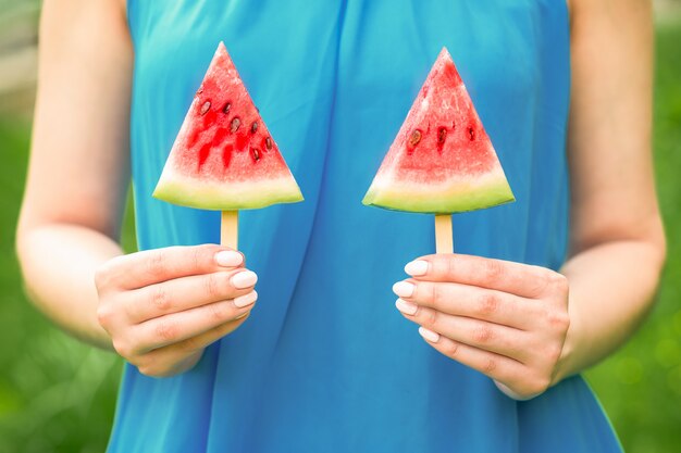 Wassermelone auf zwei Stöcken in ihren Händen des Weibchens auf einem blauen Kleidhintergrund.