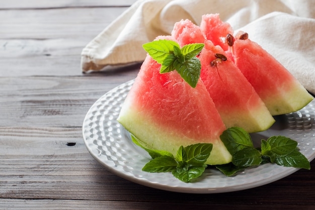 Wassermelone geschnitten auf einer Platte mit tadellosen Blättern auf einem hölzernen Hintergrund.