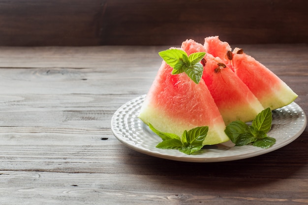 Wassermelone geschnitten auf einer Platte mit tadellosen Blättern auf einem hölzernen Hintergrund.