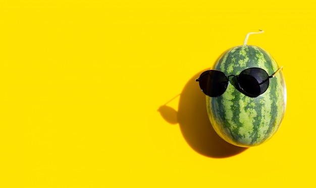 Wassermelone mit Sonnenbrille auf gelbem Hintergrund. Sommerferienkonzept genießen.