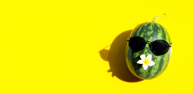 Wassermelone mit Sonnenbrille und Plumeria oder Frangipani-Blume auf gelbem Hintergrund. Speicherplatz kopieren