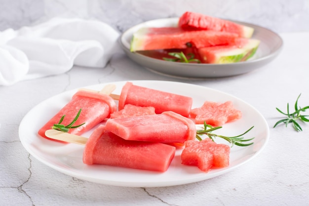 Wassermeloneneis am Stiel und Wassermelonenstücke auf einem Teller auf dem Tisch Hausgemachtes Dessert