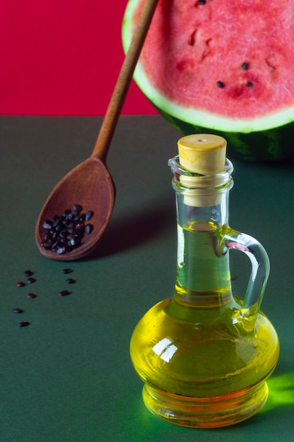 Wassermelonenkernöl in einem Glas, rohen Samen und großer Wassermelone auf rotem und grünem Hintergrund