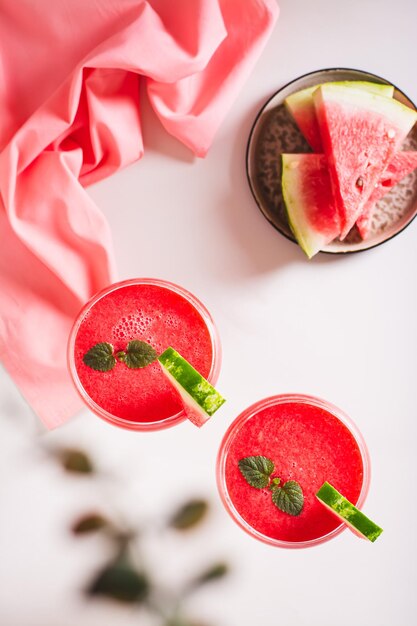 Wassermelonenlimonade mit Wassermelonenstücken in Gläsern auf rosa Hintergrund oben und vertikaler Ansicht